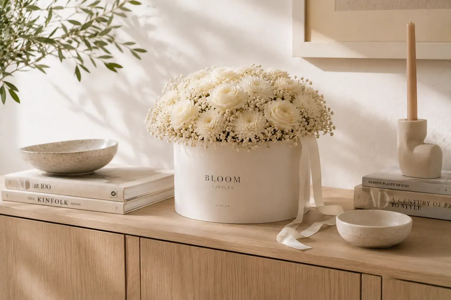 Florales Arrangement auf hellem Eichen-Sideboard zwischen Architekturbüchern, Keramikschalen und schlanker Kerze im warmen Morgenlicht — langlebiges Hochzeitsgeschenk aus Zürich im Zuhause.